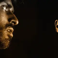 Primo piano di un uomo con barba e una donna, illuminati da una luce dorata. Un'immagine che evoca la complessità della dipendenza da sesso.