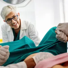 Medico sorridente assiste a un parto, tenendo la mano della paziente. Si percepisce un momento di scollamento membrane e attesa.