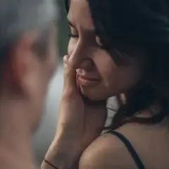 Una mano sfiora il viso di una donna, un gesto che rivela il profondo significato psicologico di una carezza: conforto, amore e connessione.