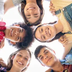 Un gruppo di amici sorride guardando verso l'alto, un'immagine che cattura la gioia e l'energia dell'adolescenza età.