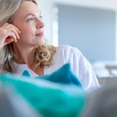 Donna bionda con mano sul viso, pensierosa. Si interroga a che età si va in menopausa, un momento di transizione.