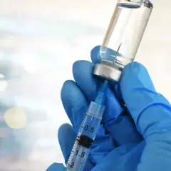 Mano guantata blu aspira liquido da fiala. Preparazione vaccino herpes zoster, attenzione agli effetti collaterali.
