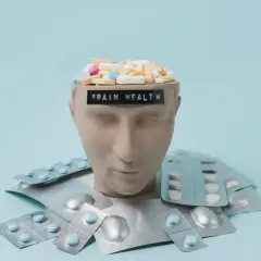 Testa di manichino piena di pillole, con blister intorno. La scritta "BRAIN HEALTH" suggerisce che gli psicofarmaci danneggiano il cervello.