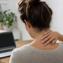 Donna con mano sul collo, laptop e tazza sul tavolo. Potrebbe soffrire di cervicale sintomi.