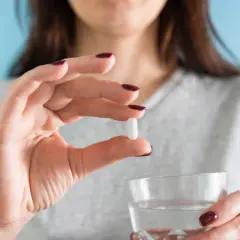 Donna tiene una pillola bianca, forse per il colesterolo, e un bicchiere d'acqua. Torvast a cosa serve?