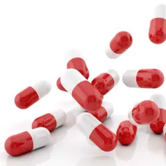 Capsule rosse e bianche, utili come cortisone per mal di gola, sparse su sfondo bianco.