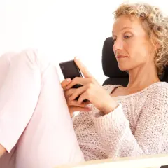 Donna bionda con capelli ricci, seduta su una poltrona, guarda il suo smartphone. Un'immagine che ispira su come superare una separazione a 50 anni.