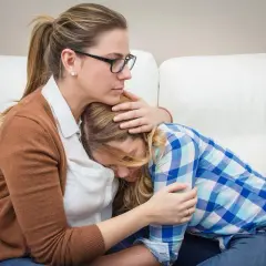 Madre abbraccia figlia in lacrime, offrendo conforto. Un gesto d'amore che può aiutare a superare le cause dell'anoressia.