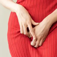 Mani che si stringono sul vestito rosso, un gesto che può indicare disagio, forse legato alla candida o al ciclo mestruale.