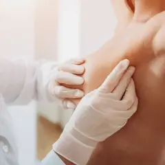 Mani guantate di un medico esaminano un seno, un'immagine che ricorda l'importanza di riconoscere i sintomi del tumore al seno.