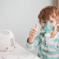 Bambino con maschera per aerosol, pollice in su. L'aerosol è pronto, prima o dopo i pasti, per respirare meglio.