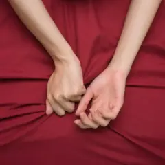 Mani intrecciate su lenzuola rosse, un simbolo di passione intensa, a volte legata al disturbo bipolare e all'ipersessualità.