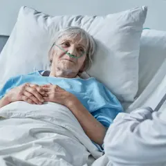 Anziana paziente in ospedale con cannula nasale, che sembra accettare la morte con serenità, mentre un medico le parla.