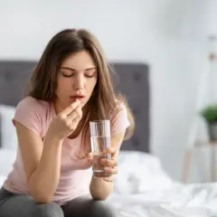 Donna con un bicchiere d'acqua e una pastiglia, forse Efferalgan 1000, per alleviare un malessere.