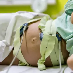 Pancia di donna incinta con monitoraggio per il parto indotto. Le fasce verdi e i sensori sono posizionati per monitorare il battito cardiaco del feto.