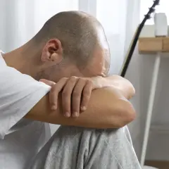 Uomo con la testa tra le braccia, in un momento di profonda riflessione e elaborazione del lutto.