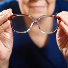 Mani anziane tengono occhiali. Domanda: quanto tempo aspettare per fare occhiali dopo intervento cataratta?