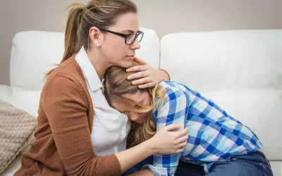 Madre abbraccia figlia in lacrime, offrendo conforto. Un gesto d'amore che può aiutare a superare le cause dell'anoressia.