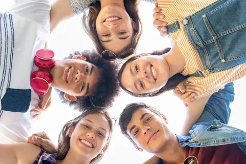 Un gruppo di amici sorride guardando verso l'alto, un'immagine che cattura la gioia e l'energia dell'adolescenza età.