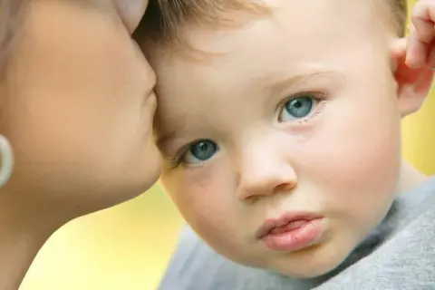 Un bambino con autismo e paura degli estranei piange mentre riceve un bacio rassicurante dalla madre.