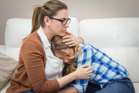 Madre abbraccia figlia in lacrime, offrendo conforto. Un gesto d'amore che può aiutare a superare le cause dell'anoressia.