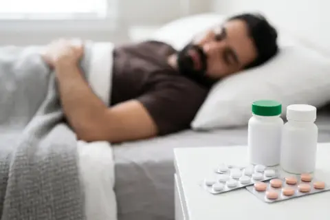 Uomo addormentato a letto, con blister di pillole e flaconi sul comodino. Cosa sono i barbiturici?