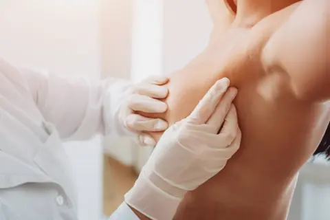Mani guantate di un medico esaminano un seno, un'immagine che ricorda l'importanza di riconoscere i sintomi del tumore al seno.