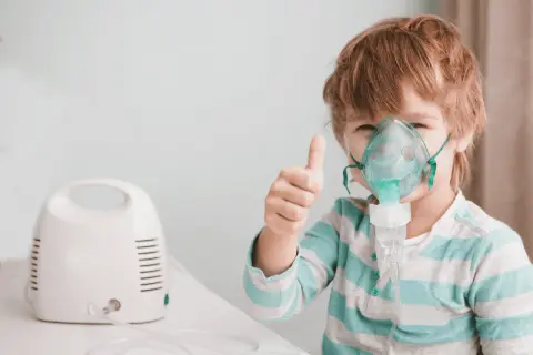 Bambino con maschera per aerosol, pollice in su. L'aerosol è pronto, prima o dopo i pasti, per respirare meglio.