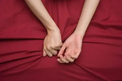 Mani intrecciate su lenzuola rosse, un simbolo di passione intensa, a volte legata al disturbo bipolare e all'ipersessualità.