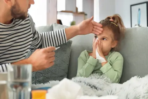 Padre controlla la febbre alla figlia, che soffia il naso, mostrando i tipici adenovirus sintomi.