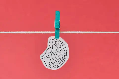 Un cervello stilizzato, appeso a un filo con una molletta turchese, evoca un effetto Flynn inverso, suggerendo un declino intellettuale.