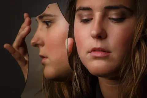 Ragazza con volto riflesso in uno specchio rotto, un'immagine che evoca cosa fa arrabbiare un bipolare.
