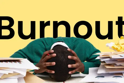 Persona con la testa tra le mani, circondata da pile di documenti, con la parola "Burnout" in grande sullo sfondo giallo. Sintomi di esaurimento.