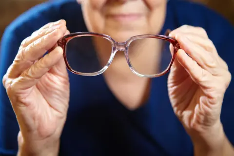 Mani anziane tengono occhiali. Domanda: quanto tempo aspettare per fare occhiali dopo intervento cataratta?