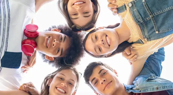 Un gruppo di amici sorride guardando verso l'alto, un'immagine che cattura la gioia e l'energia dell'adolescenza età.