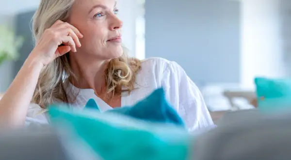 Donna bionda con mano sul viso, pensierosa. Si interroga a che età si va in menopausa, un momento di transizione.