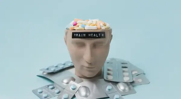 Testa di manichino piena di pillole, con blister intorno. La scritta "BRAIN HEALTH" suggerisce che gli psicofarmaci danneggiano il cervello.