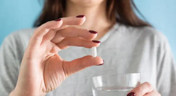 Donna tiene una pillola bianca, forse per il colesterolo, e un bicchiere d'acqua. Torvast a cosa serve?