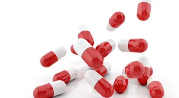 Capsule rosse e bianche, utili come cortisone per mal di gola, sparse su sfondo bianco.