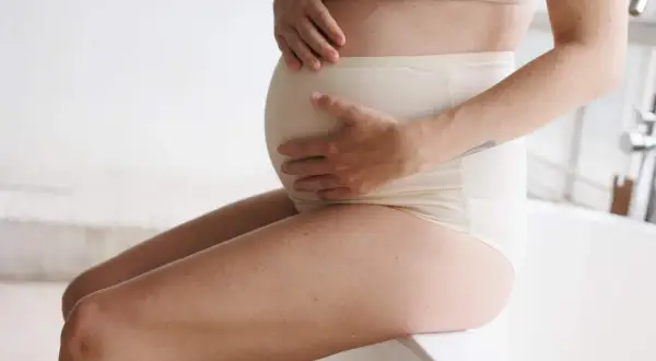 Donna incinta con mani sul pancione, che affronta la stitichezza in gravidanza.