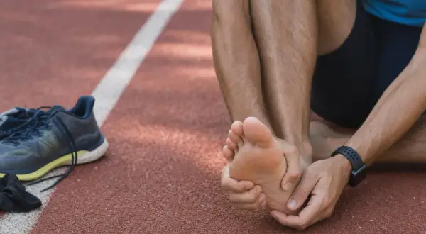 Atleta seduto su una pista, si tiene il piede destro, lamentando un forte bruciore ai piedi dopo la corsa. Scarpe da ginnastica a sinistra.