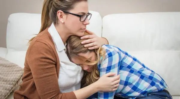 Madre abbraccia figlia in lacrime, offrendo conforto. Un gesto d'amore che può aiutare a superare le cause dell'anoressia.