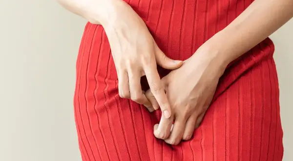 Mani che si stringono sul vestito rosso, un gesto che può indicare disagio, forse legato alla candida o al ciclo mestruale.
