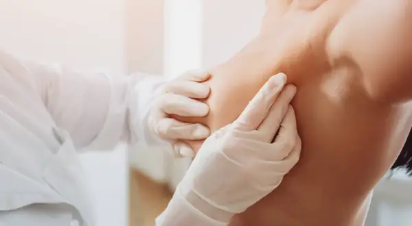 Mani guantate di un medico esaminano un seno, un'immagine che ricorda l'importanza di riconoscere i sintomi del tumore al seno.