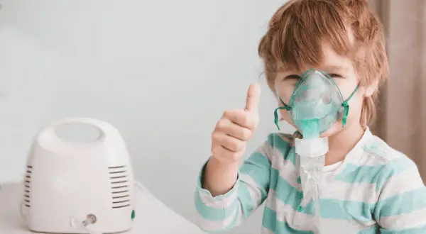 Bambino con maschera per aerosol, pollice in su. L'aerosol è pronto, prima o dopo i pasti, per respirare meglio.