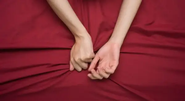 Mani intrecciate su lenzuola rosse, un simbolo di passione intensa, a volte legata al disturbo bipolare e all'ipersessualità.