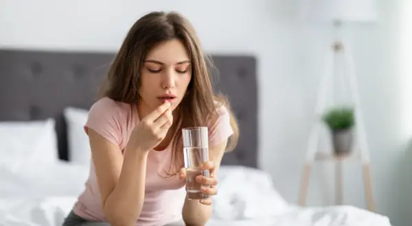 Donna con un bicchiere d'acqua e una pastiglia, forse Efferalgan 1000, per alleviare un malessere.