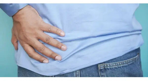 Mano appoggiata sul fianco sinistro, indicando un possibile dolore.