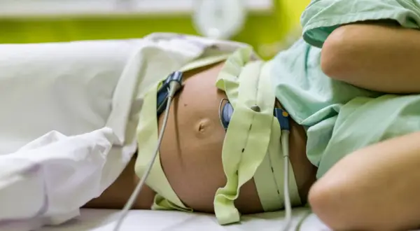 Pancia di donna incinta con monitoraggio per il parto indotto. Le fasce verdi e i sensori sono posizionati per monitorare il battito cardiaco del feto.