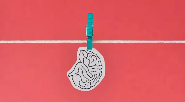 Un cervello stilizzato, appeso a un filo con una molletta turchese, evoca un effetto Flynn inverso, suggerendo un declino intellettuale.